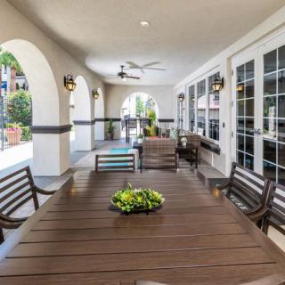 A cozy outdoor patio with a large dining table, surrounded by chairs and decorated with plants.