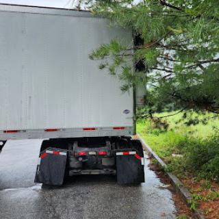 A rear view of a parked truck beside a tree-lined area.