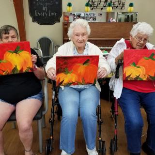 A group of seniors proudly displaying their autumn-themed paintings during a group art activity.