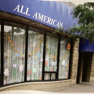 A storefront with a blue awning reading 'All American' and decorated windows.