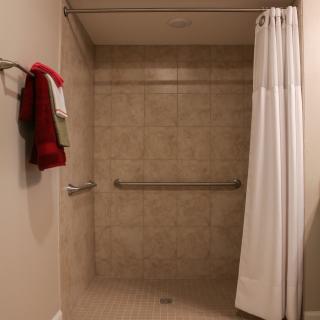 A bathroom shower with a white curtain, beige tiled walls, and a grab bar for support.