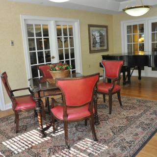 A well-designed dining room featuring red upholstered chairs, a wooden table, and a grand piano on a patterned rug.