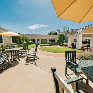 A sunny outdoor patio area with tables, chairs, and umbrellas surrounded by a well-maintained garden.