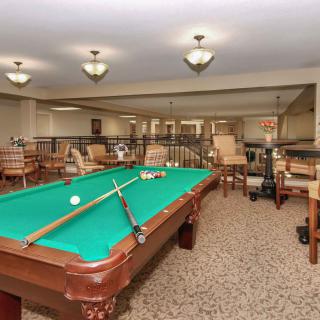 A cozy recreation room featuring a billiards table, surrounded by comfortable seating and warm lighting.