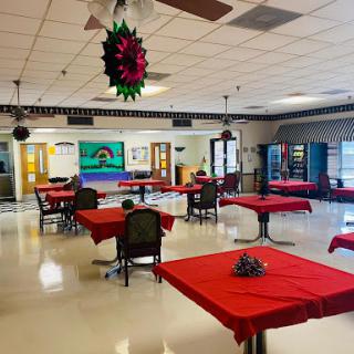 A spacious dining area set up with red tablecloths, featuring a few tables and vending machines in the background.