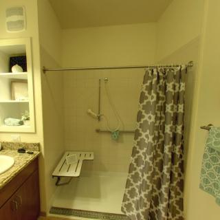 A bathroom featuring a shower with grab bars and a folding seat for accessibility.
