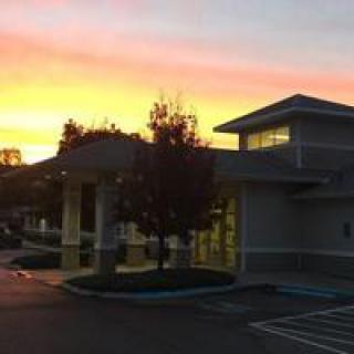 A building next to a parking lot at sunset, with trees silhouetted against the colorful sky.
