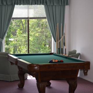 A pool table in a room with large windows and green curtains.