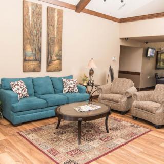 A cozy living room featuring a blue sofa, two beige armchairs, and a wooden coffee table atop a patterned rug. The room is decorated with wall art and has hardwood flooring.