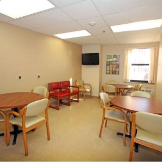 A well-lit waiting room with tables and chairs, featuring a wall-mounted television.
