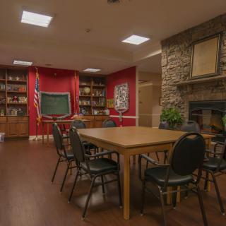 A cozy library meeting room with bookshelves, a central table surrounded by chairs, and a fireplace.