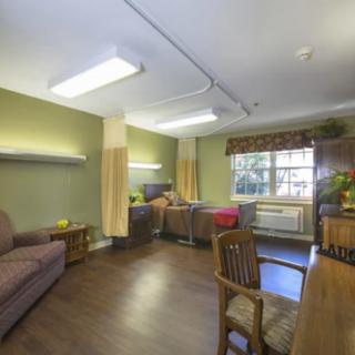 A hospital room with beds, furniture, and a large window.