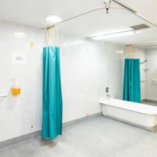 A sterile hospital bathroom featuring a bathtub and teal shower curtain.