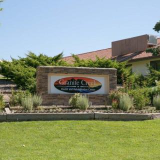 A landscaped entrance sign with greenery and a building in the background on a sunny day.