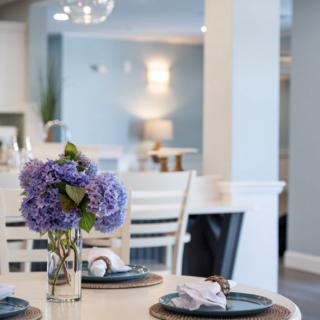 A modern dining area with a vase of purple flowers as the centerpiece, surrounded by elegant table settings.