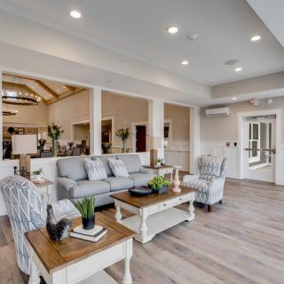 A modern living room with elegant furniture, featuring a sofa and coffee tables on wooden flooring under bright lighting.