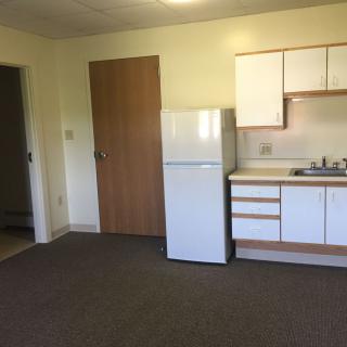 A small kitchen area in an empty apartment with a fridge and sink.
