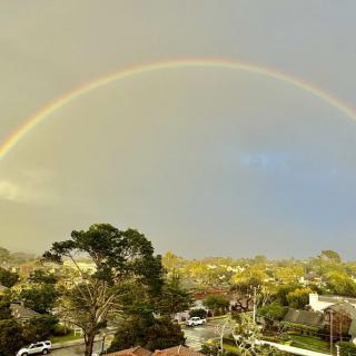 A vibrant rainbow arches over a scenic neighborhood landscape.