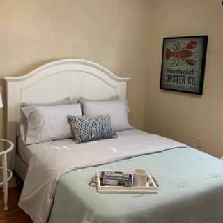 A cozy and neatly arranged bedroom with a white bed, decorative pillows, a bedside lamp, and framed artwork on the wall.
