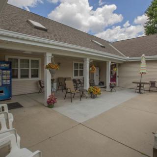 A cozy outdoor patio area with tables and chairs, surrounded by flowers and a vending machine against the building.