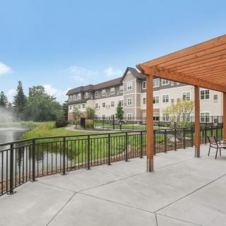 A scenic view of a building near a pond, with an outdoor seating area under a wooden pergola.