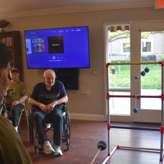 A group of people gather indoors, with one person in a wheelchair near a ladder toss game setup.