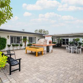 A spacious outdoor patio with a brick oven, seating area, and paved flooring.