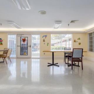 An interior room with tables, chairs, and large windows providing natural light.