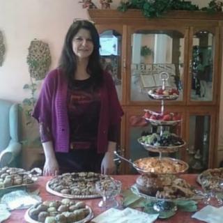 A woman standing by a table with a variety of desserts and food.