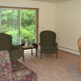 A cozy living room with green chairs, a floral sofa, and a coffee table by a large window.