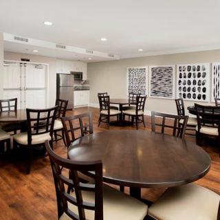 A neatly arranged dining room with round wooden tables and cushioned chairs, featuring artwork on the walls.
