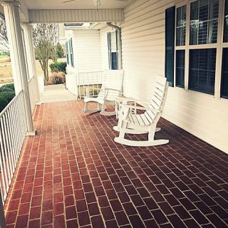 A cozy porch with a brick floor and white rocking chairs.