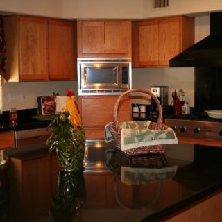 A modern kitchen with wooden cabinets and a black countertop, featuring a basket and various appliances.