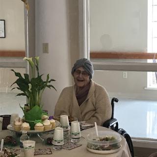 An elderly woman enjoying a meal at a beautifully set table in a bright indoor space.