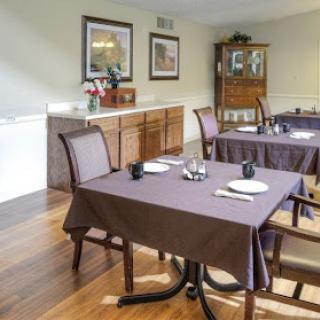 A cozy dining room setup featuring wooden tables and chairs with brown tablecloths, complemented by wall decorations and a decorative cabinet.