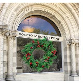 An arched window of 'Kokoro Assisted Living' adorned with a festive holiday wreath.