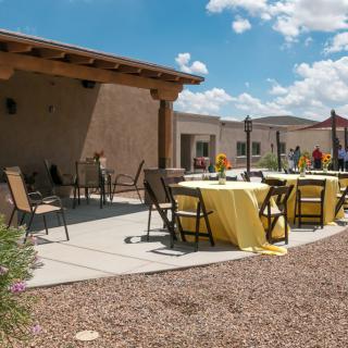 A sunny outdoor patio with tables covered in yellow tablecloths and chairs arranged for an event.