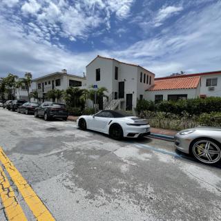 A row of parked cars in front of residential buildings under a cloudy sky.