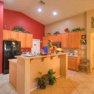 A modern kitchen with wood cabinets and an island counter, featuring appliances and decorative elements under warm lighting.