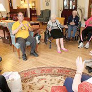 A group of elderly individuals sitting in a circle during a social gathering in a living room setting.