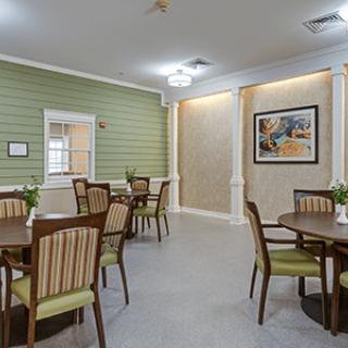 A neatly arranged dining area with several tables and chairs, featuring green walls and artwork.