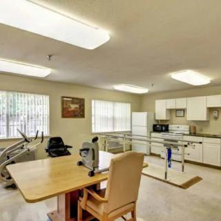 A rehabilitation room equipped with exercise machines and a kitchen area for physical therapy exercises.