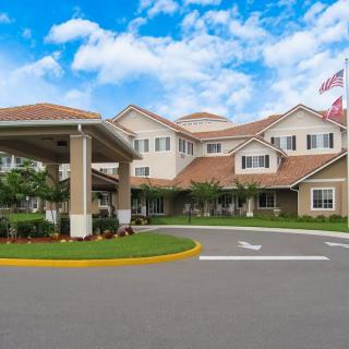 A well-maintained residential building with an entrance driveway and flags flying against a partly cloudy sky.