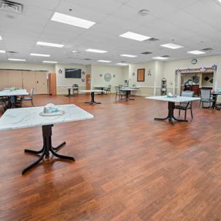 A spacious and well-lit indoor dining area featuring several empty tables on a wooden floor.