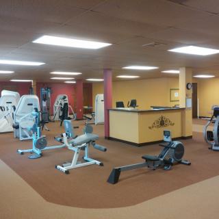 A well-lit gym with various exercise machines and a reception desk.