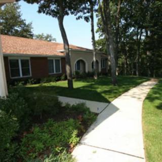 A suburban house with a walkway surrounded by trees and well-maintained landscaping.