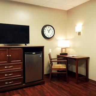 A cozy hotel room corner with a television, mini fridge, and a work desk.