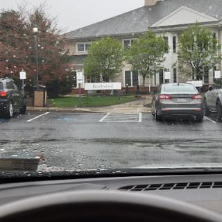 A view from inside a vehicle showing a rainy parking lot in front of an apartment complex.