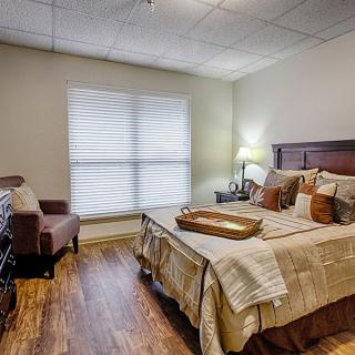 A cozy bedroom with a neatly made bed, wooden floors, and soft ambient lighting.