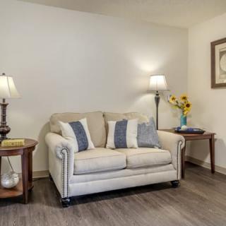 A cozy living room with a beige sofa, accented by blue and white cushions, flanked by two wooden tables and lamps.